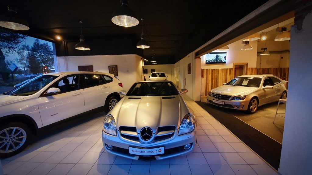 De showroom van Automobiel Limburg aan de Handelsstraat in Sittard met occasions en het kentekenplaat-logo aan de wand